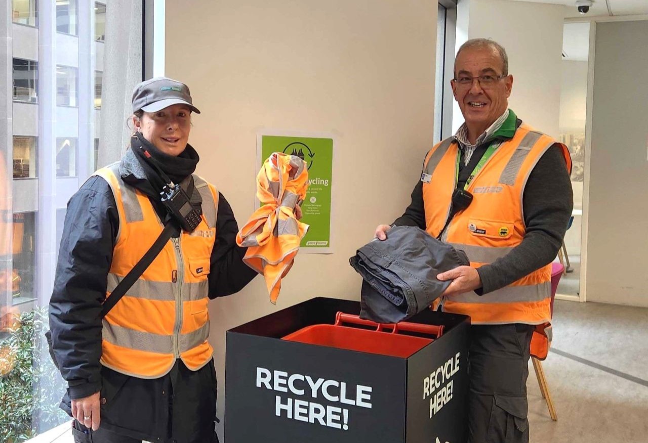 Two Yarra Tram employees pose infront of a uniform recycling bin with 