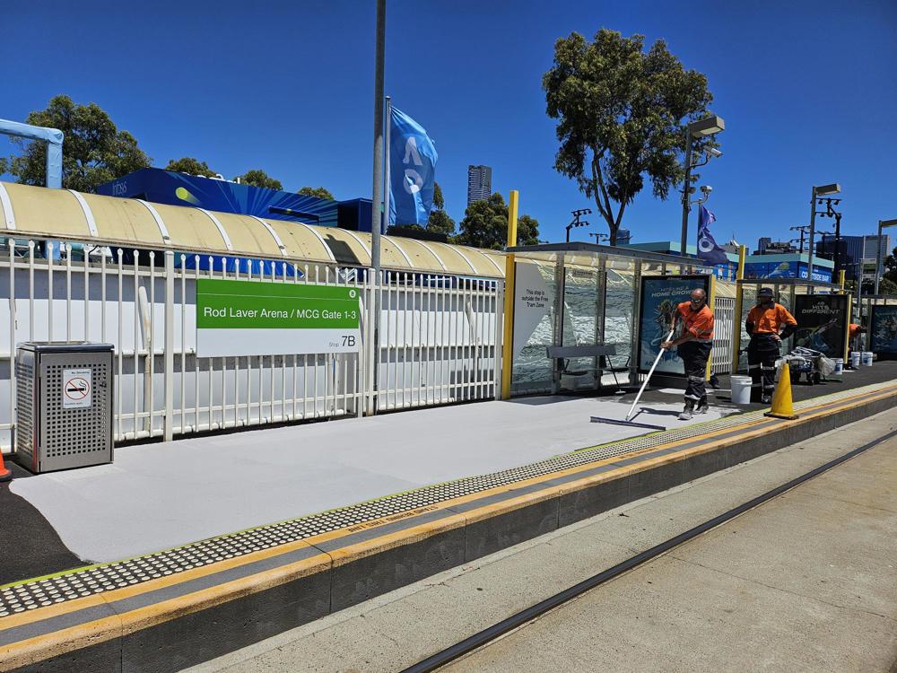 Photo of Rod Laver Arena stop, with a light coloured paint being applied to the asphalt
