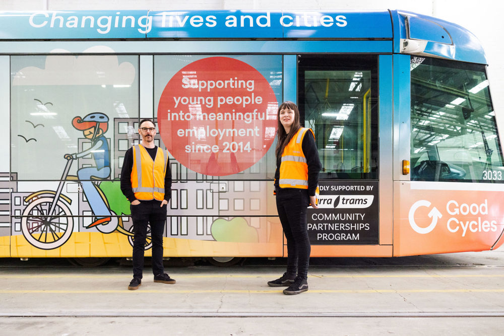 Photo: Two members from Good Cycles stand next to their community partnerships tram